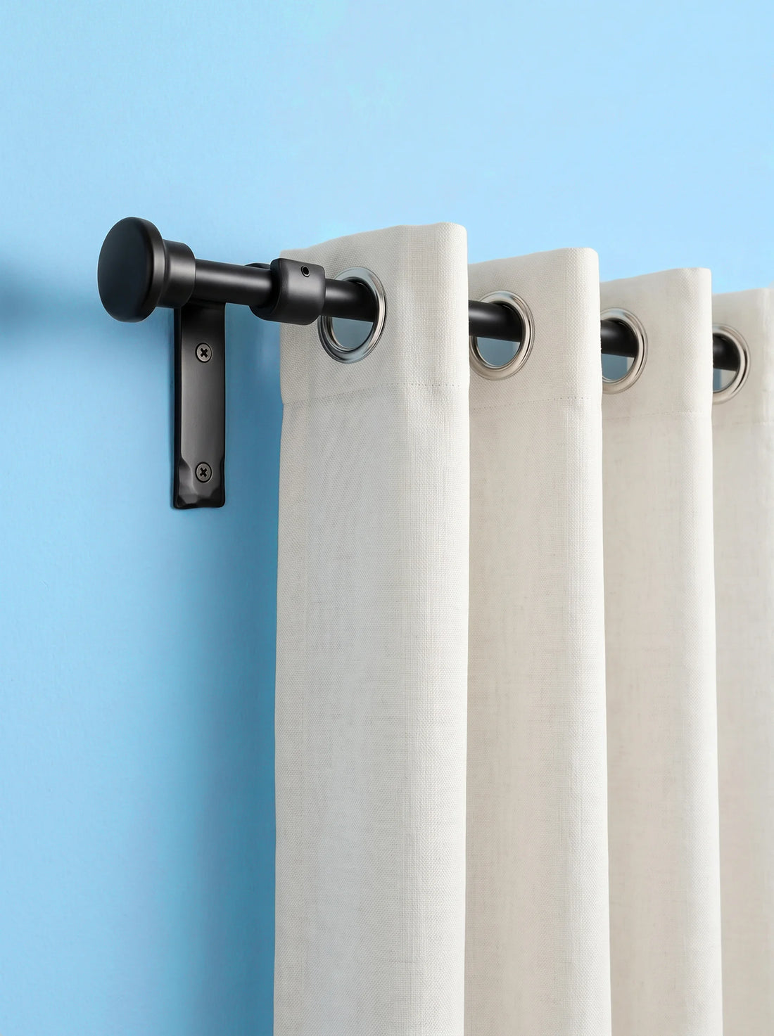 A close-up of a curtain rod with a wall bracket holding off a light beige grommet curtain against a solid light blue wall.