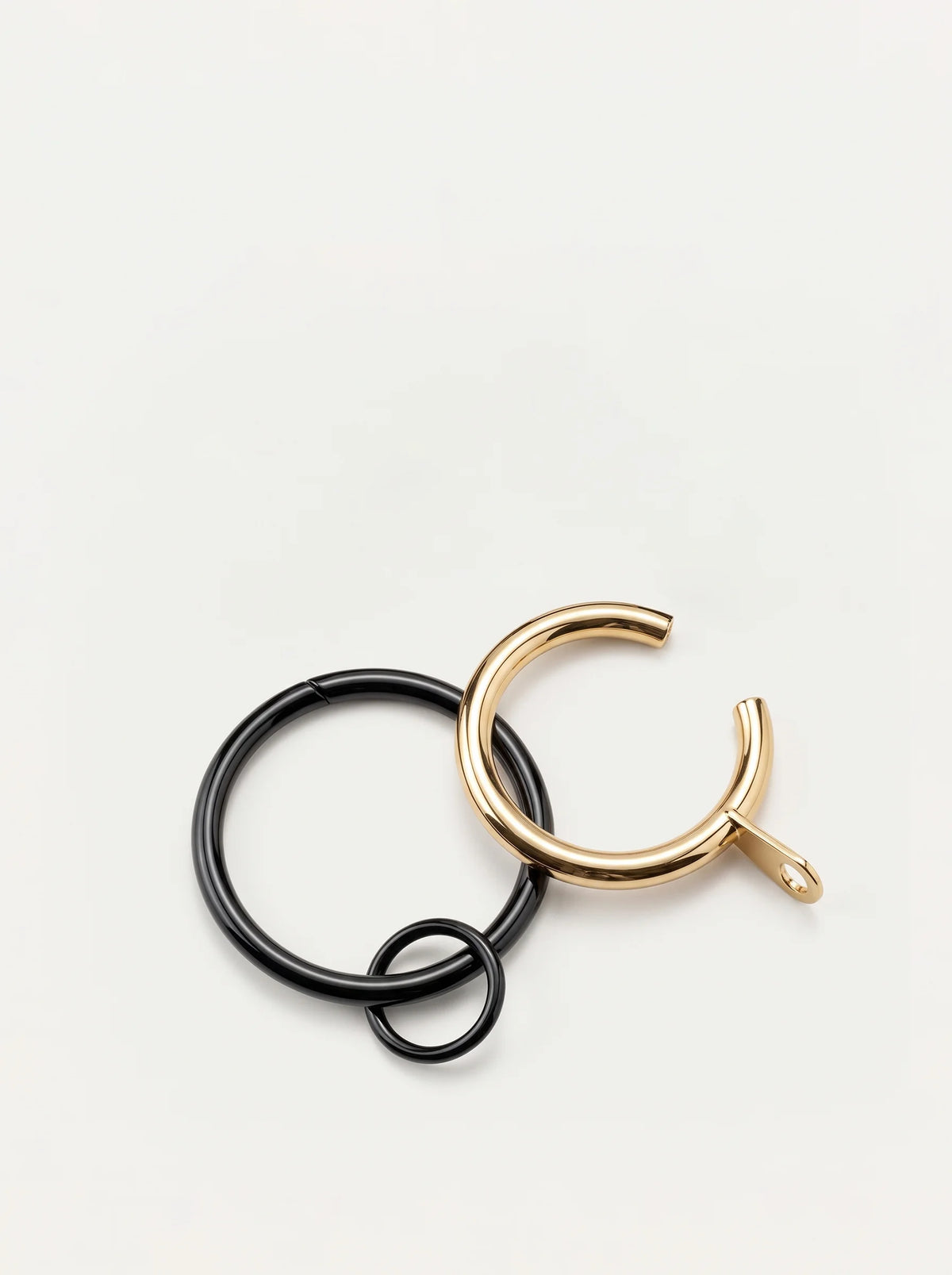 A pair of minimalist open hoop earrings, one in matte black and one in polished gold, interlocking on a clean white background.