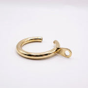 A polished gold-colored metal cuff bracelet with a flat tab and circular hole on one end, displayed on a clean white background.