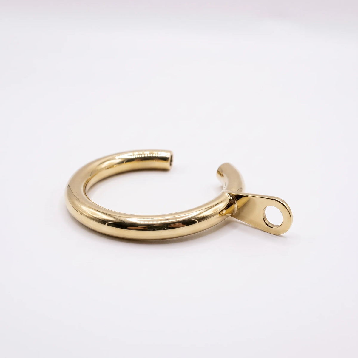 A polished gold-colored metal cuff bracelet with a flat tab and circular hole on one end, displayed on a clean white background.
